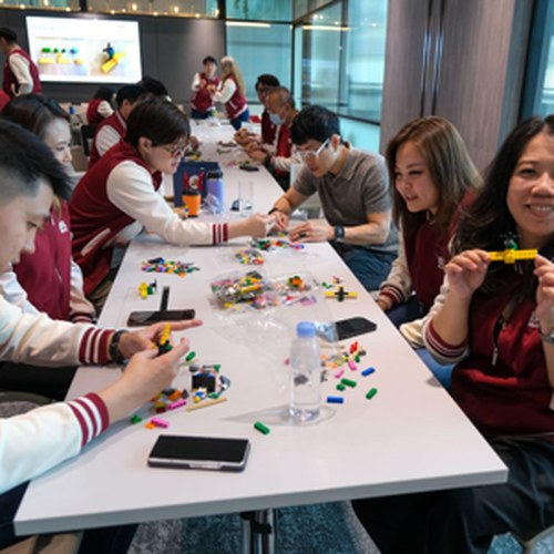 Team members building and sharing their LEGO models around a long table